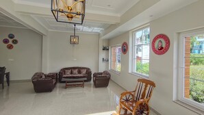Un salon spacieux avec un plafond haut, un lustre, un ensemble de canapés, un fauteuil à bascule et de grandes fenêtres ornées d’assiettes décoratives accrochées aux murs.