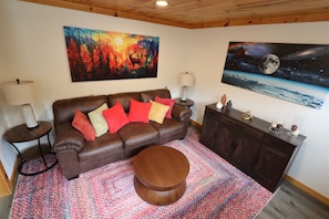 A living room with a brown leather sofa, colorful pillows, a round wooden coffee table, and two paintings on the walls.