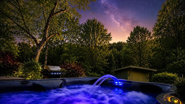 Un jacuzzi con un cielo estrellado y una parrilla en un área boscosa.