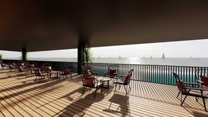 Une terrasse avec des sièges extérieurs, une vue sur la mer et des voiliers à l’horizon.