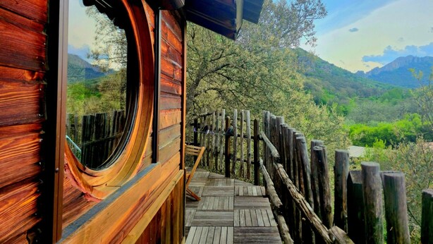 A wooden cabin with a circular window and a wooden deck leading to a scenic mountain view. - gites o fil de l'eau (Omessa)