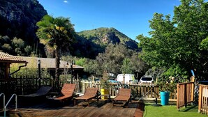 A pool area with wooden deck chairs, a small building with a tiled roof, and a mountain in the background. - gites o fil de l'eau (Omessa)