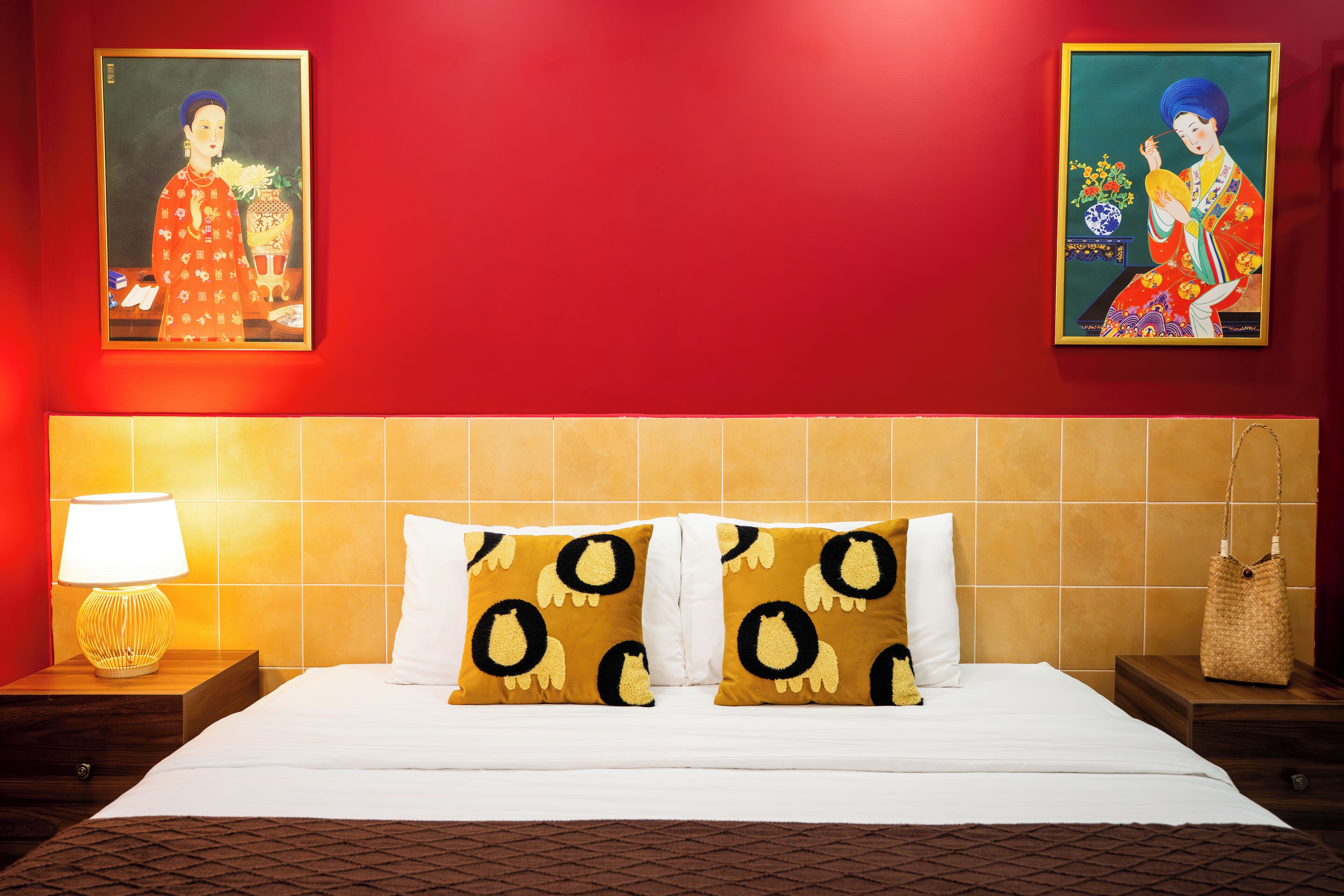 Une chambre d’hôtel avec un grand lit, deux oreillers à motifs circulaires, une table de chevet avec une lampe et deux tableaux au mur.