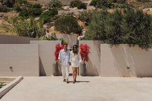 A couple walking on a flat, paved surface with a low wall and potted plants in the background. - Mitos Ultimate Escape Villa (Naxos)