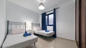A bedroom with two beds, a nightstand, a lamp, and a window with curtains. - El rincón de famara - By LVH (Famara)