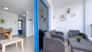 A modern living room with grey wicker furniture, a wooden table with pencils, and a blue-framed door leading to another room. - El rincón de famara - By LVH (Famara)