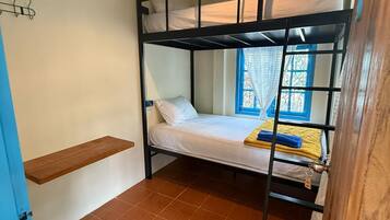 A bunk bed room with a hanging light fixture, a small wooden stool, and a window with blue shutters.