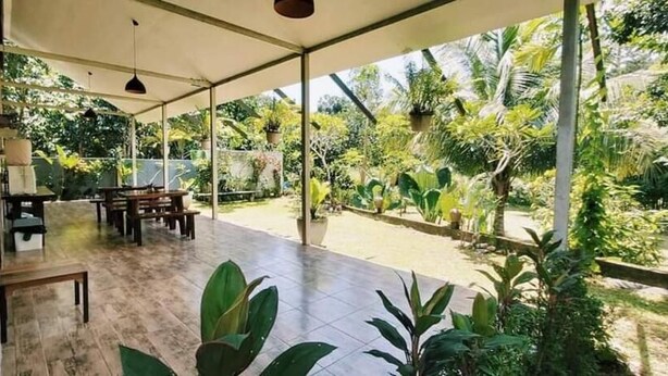 A covered patio with a dining area, surrounded by lush greenery and a view of a garden. - Baan Hinlad Home and Hostel (Koh Samui)