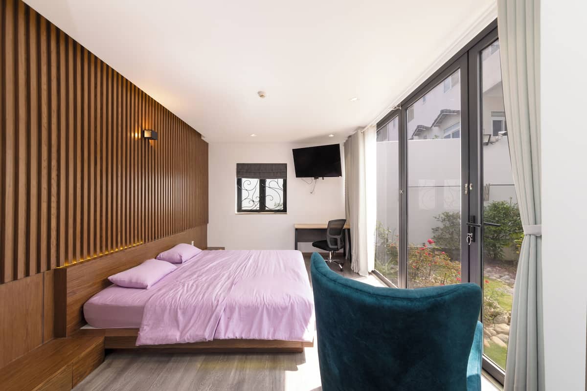 A modern bedroom with a bed, a desk, a chair, a TV, and a large window.