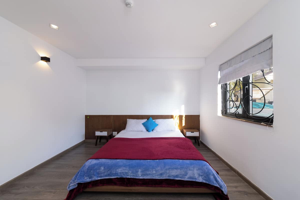 A bedroom with a bed, bedside tables, a window with a view, and a ceiling light.
