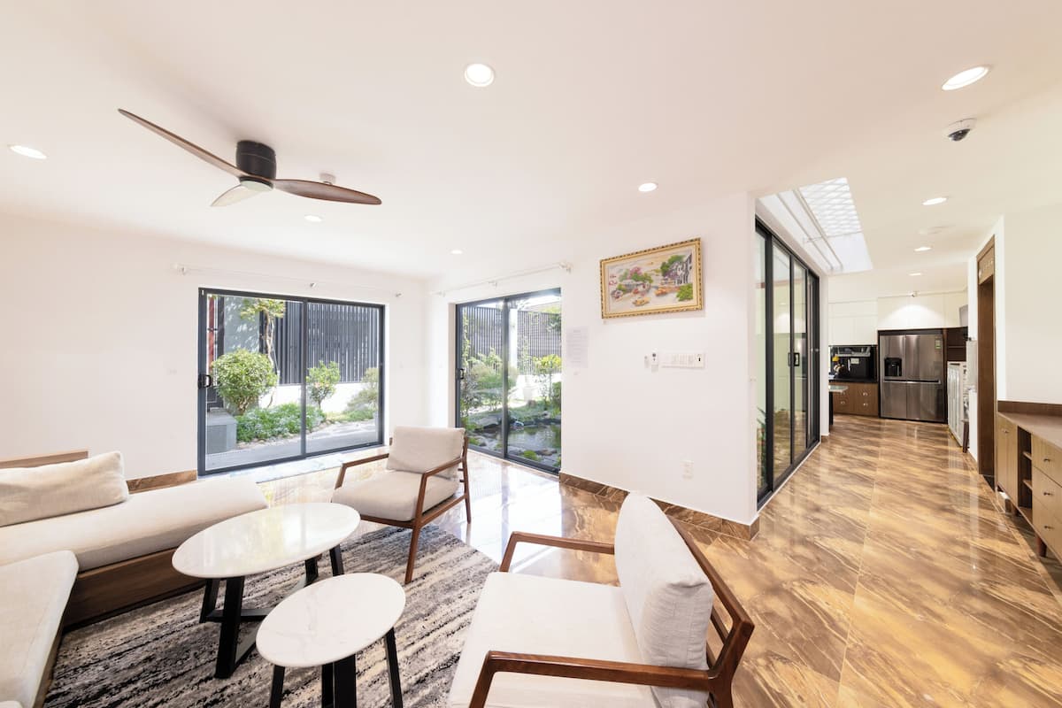 A modern living room with a sofa, chairs, a coffee table, a ceiling fan, and a kitchen in the background.