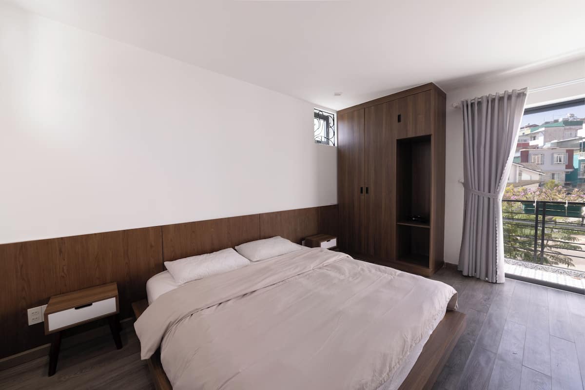 A bedroom with a bed, a nightstand, a wardrobe, and a window with curtains.