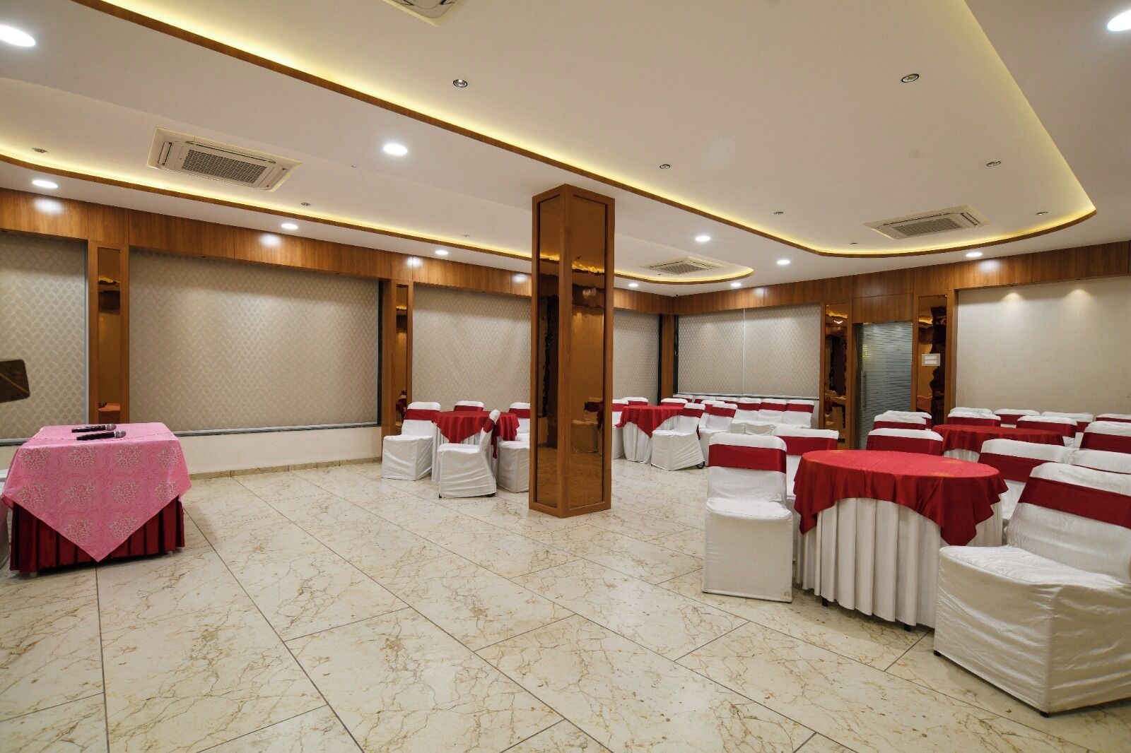 A conference room with white chairs and red sashes, a pink table, and wooden paneling on the walls.