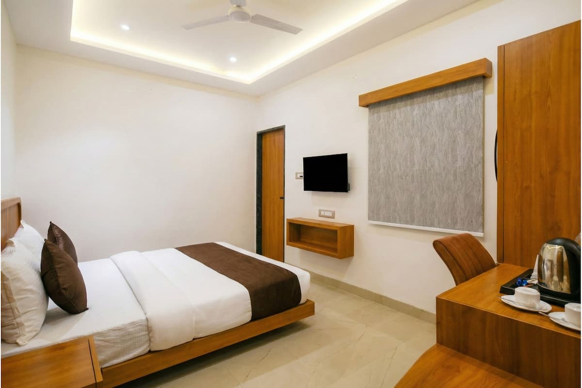 A modern hotel room with a bed, a desk, a chair, a television, and a window with a curtain.