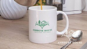 Una mano sirviendo café en una taza con el logotipo de Ashdene House.