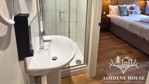 Un baño moderno con cabina de ducha de vidrio, un lavabo blanco y un secador de pelo en la pared.
