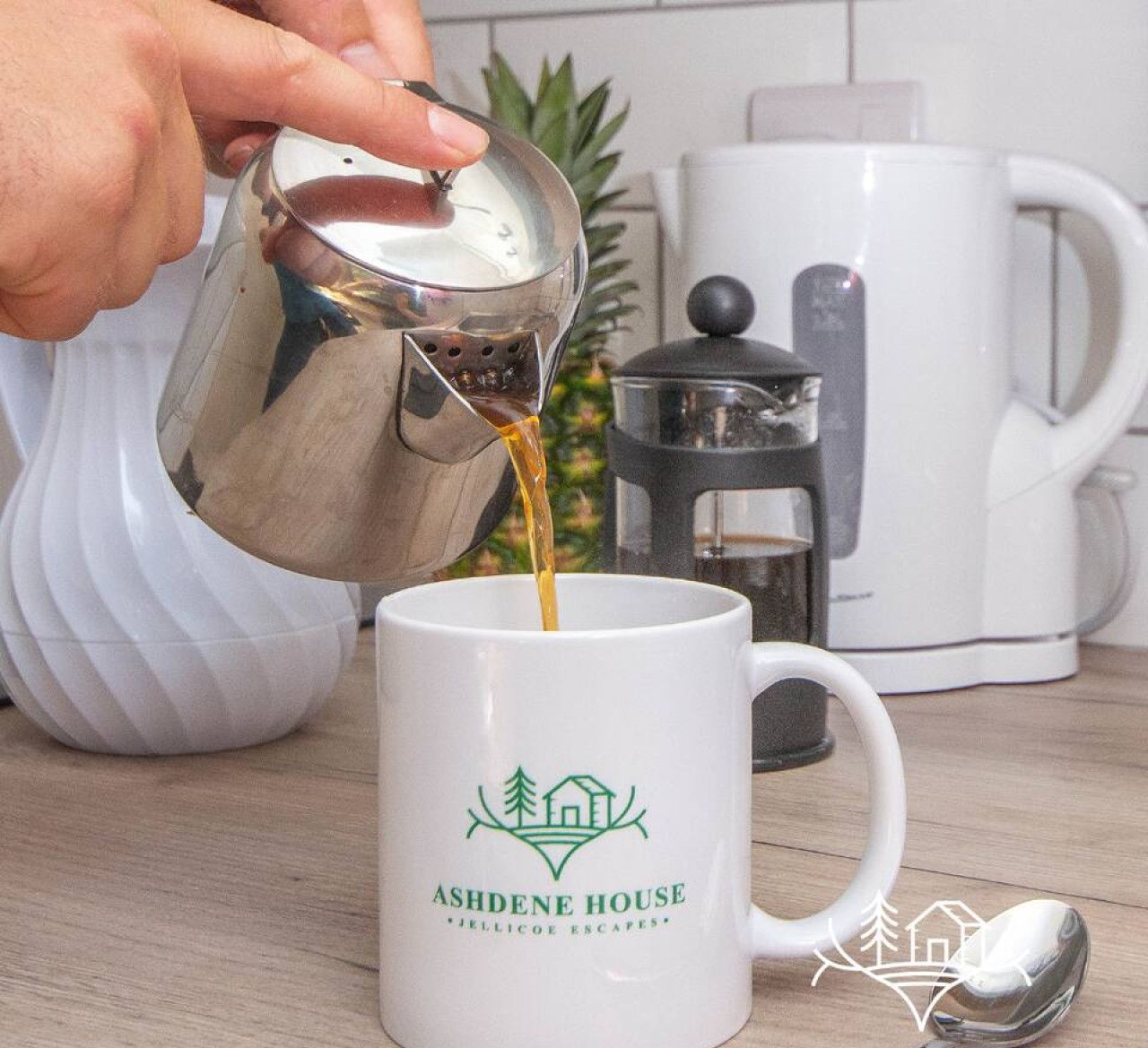Une main verse du café dans une tasse ornée du logo d’Ashdene House.