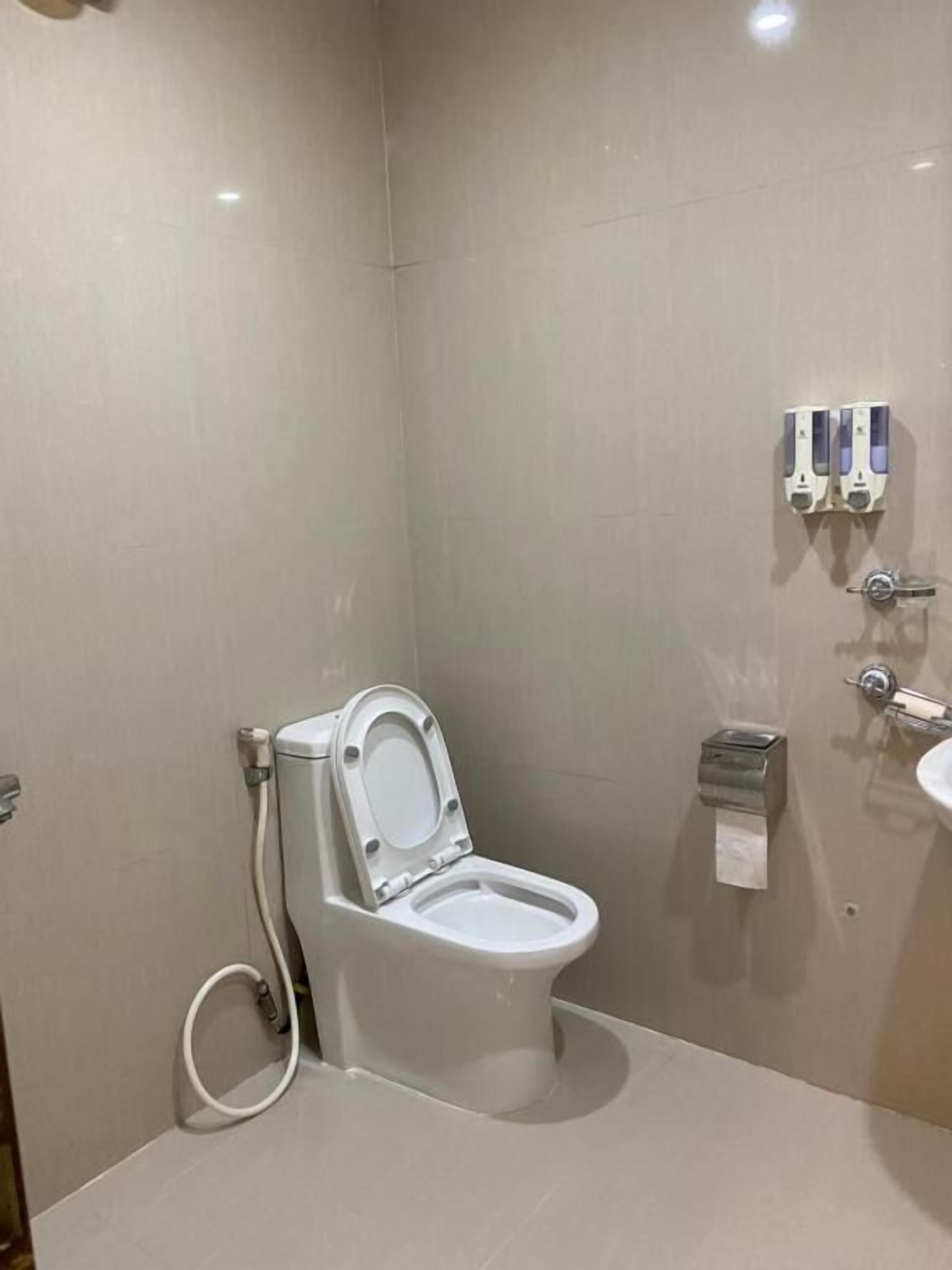 A modern bathroom with a white toilet, a hand dryer, and a paper towel dispenser.
