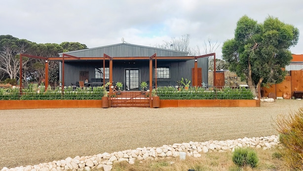 Een modern gebouw met een overdekt terras, een grindpad en een stenen rand.