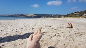 Een strand met een heldere lucht, een zandstrand en een paar voeten op de voorgrond.
