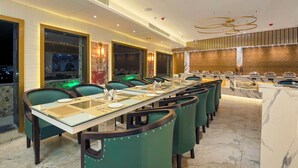 Uma sala de jantar moderna com mesas longas, cadeiras estofadas em verde e bancada de mármore.