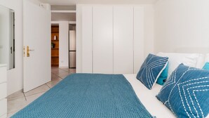 A bedroom with a bed, a blue bedspread, and matching pillows. There is a wardrobe with white doors and a small closet with a wooden door. - Studio Anid - Lecce Selection (Lecce)