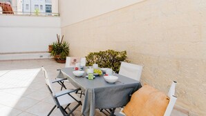 A dining table set with white plates, bowls, and a menu, surrounded by white chairs with a grey tablecloth. - Studio Anid - Lecce Selection (Lecce)