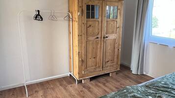 A bedroom with a wooden wardrobe, a bed with a floral bedspread, and a window with curtains.