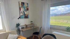 Moderni huone, jossa on puinen työpöytä, mukava tuoli, sohva ja suuri ikkuna, josta avautuu näkymä vehreälle niitylle.