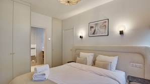 Une chambre à coucher bien rangée, avec un grand lit, une table de chevet, une armoire et une œuvre d’art encadrée accrochée au mur.