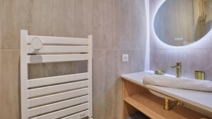 Une salle de bain moderne avec un porte-serviettes blanc, un miroir rond et un meuble-lavabo en bois doté d’un robinet doré.