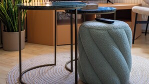 Un salon moderne avec un téléviseur à écran plat, une table basse ronde, un pouf confortable et une plante en pot.