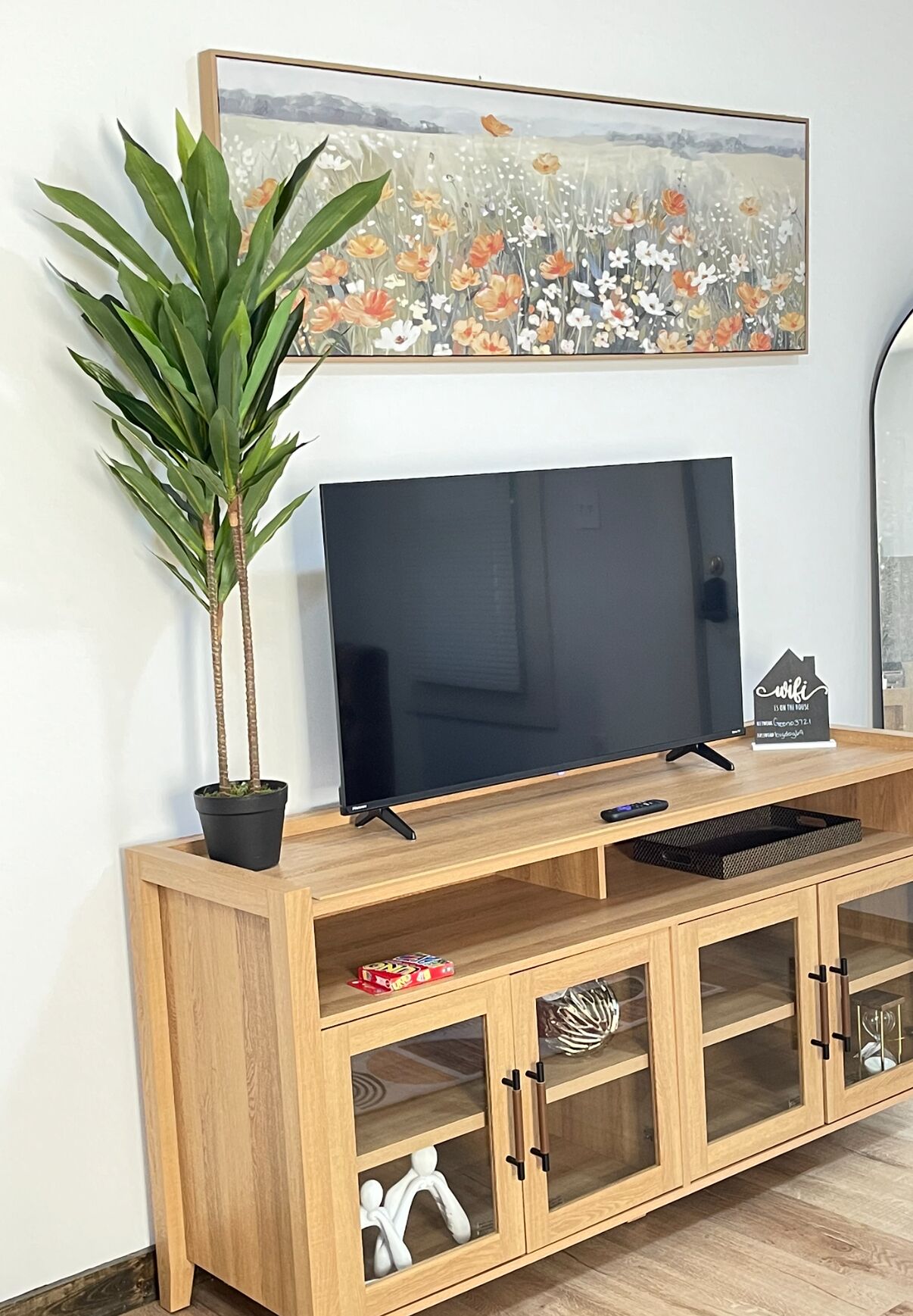 A wooden TV stand with a flat-screen TV, a potted plant, and a decorative sign.