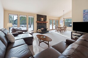 A spacious living room with leather sofas, a fireplace, a dining area with chairs, and a television. - Goldfinch 18 - A/C, Hot Tub, SHARC Passes, Near River (Sunriver)