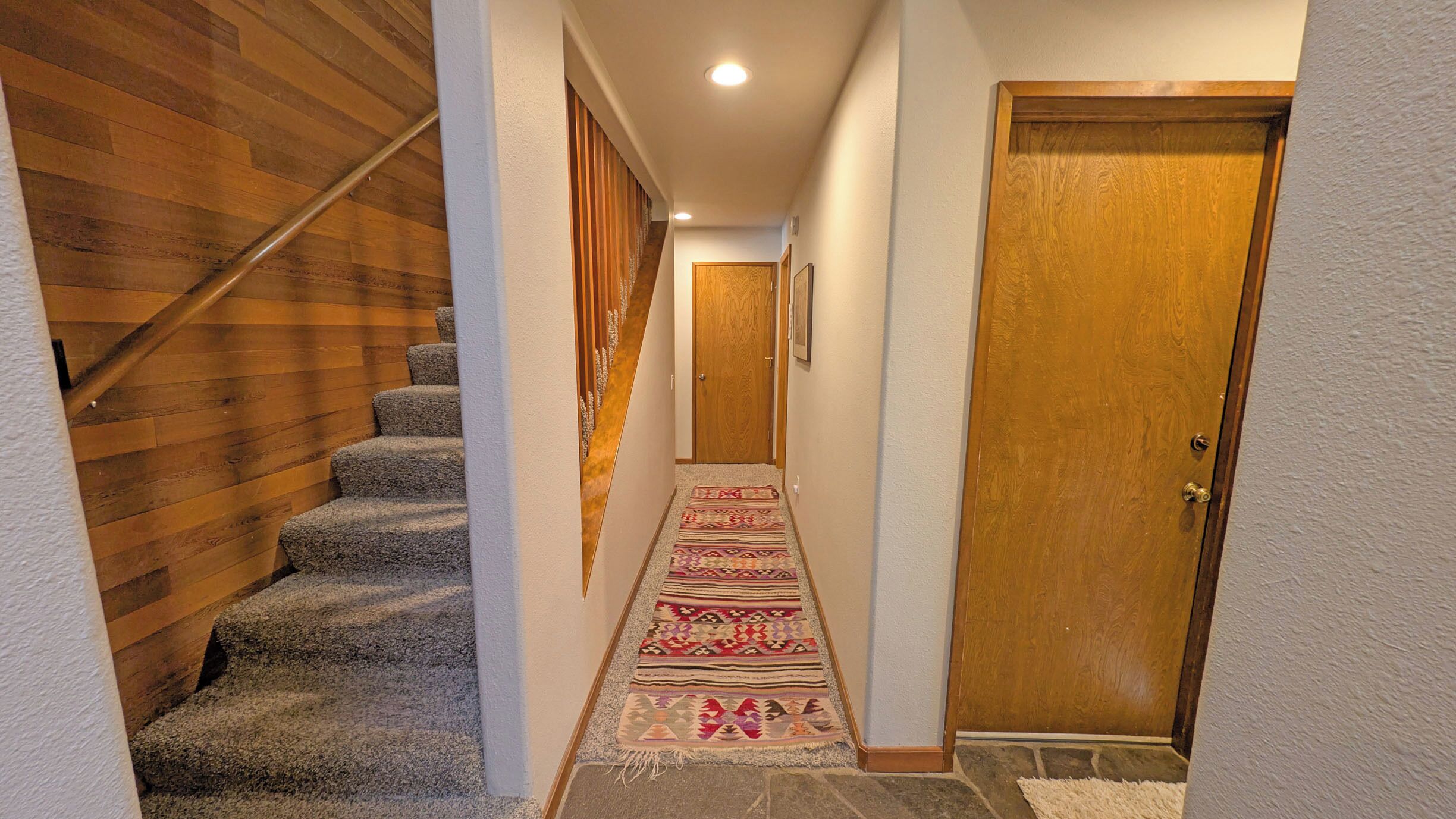 A hallway with a carpeted staircase, a wooden door, and a light-colored wall.