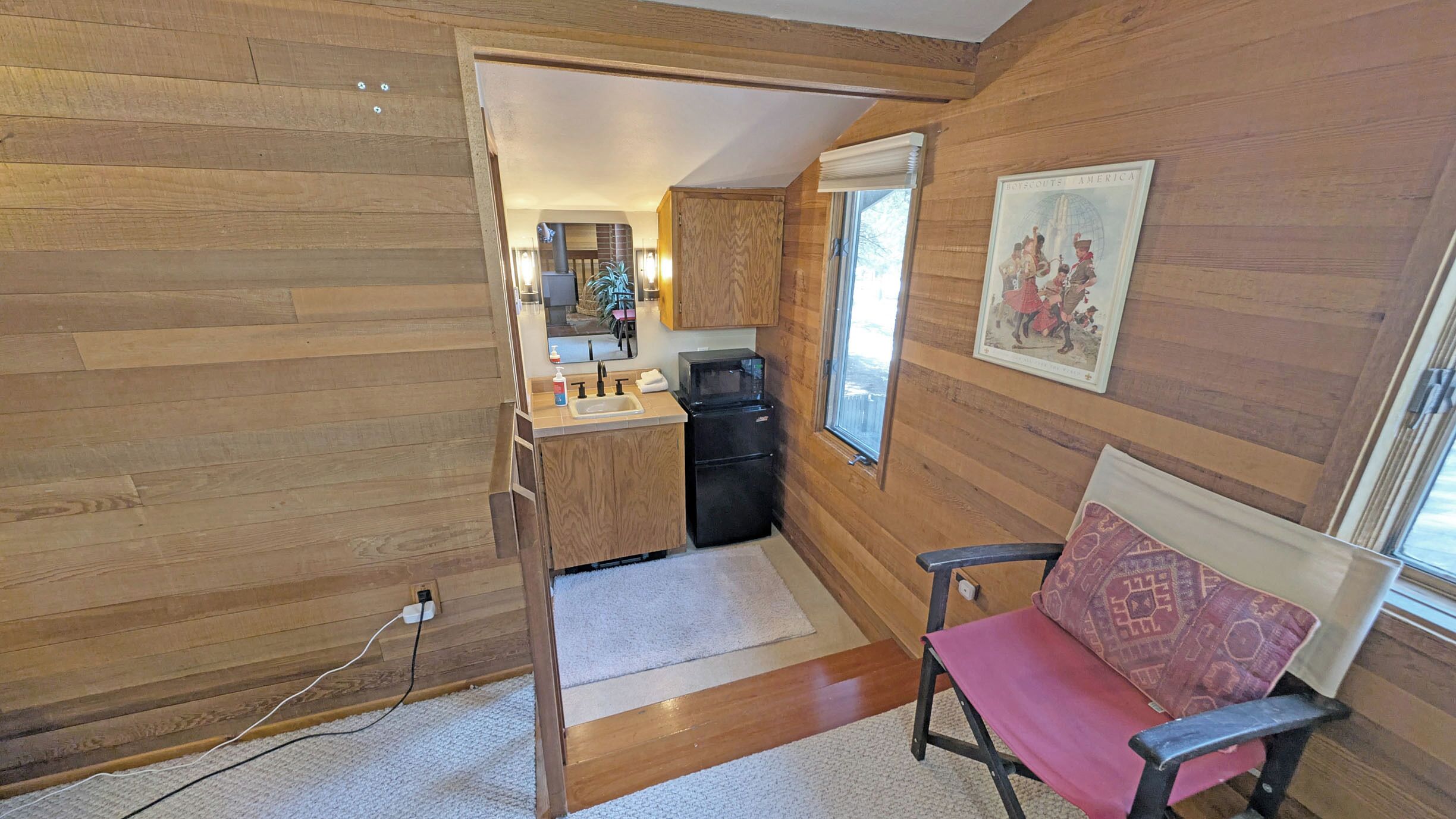 Una cocina compacta con paredes de madera, un lavamanos y un refrigerador.