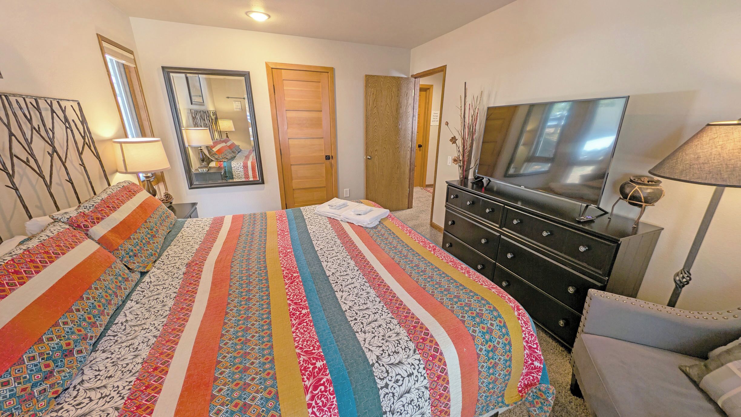 A bedroom with a large bed, a dresser, a television, and a mirror.