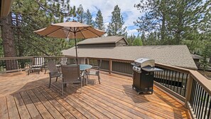 A wooden deck with a grill, chairs, and an umbrella.