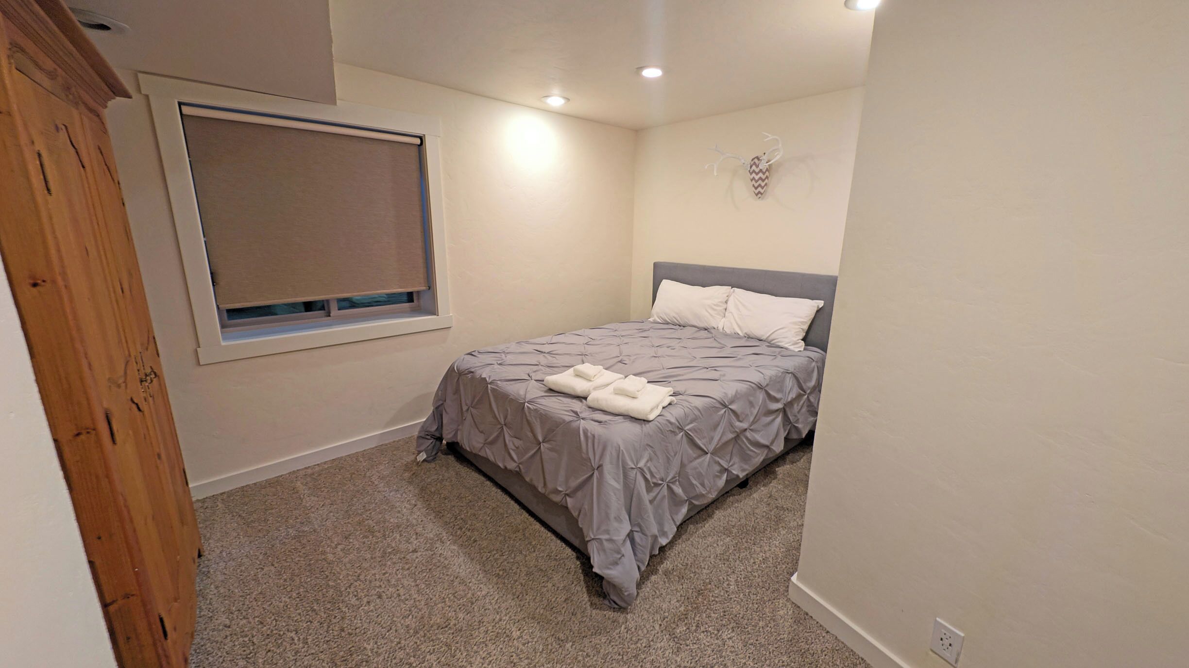 Ein Schlafzimmer mit Bett, einem Fenster mit Jalousien, einer Holztür und einer Wandleuchte.
