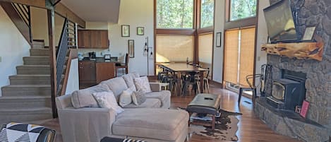 A spacious living room with a staircase, a dining area, and a stone fireplace.