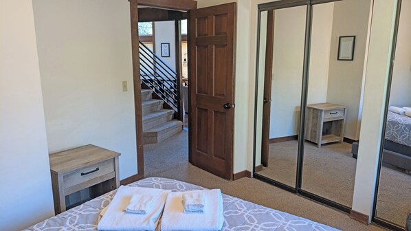 Une chambre à coucher comprenant un lit, deux tables de chevet, une commode, un banc en bois, une armoire avec un miroir et un escalier menant à une autre pièce.