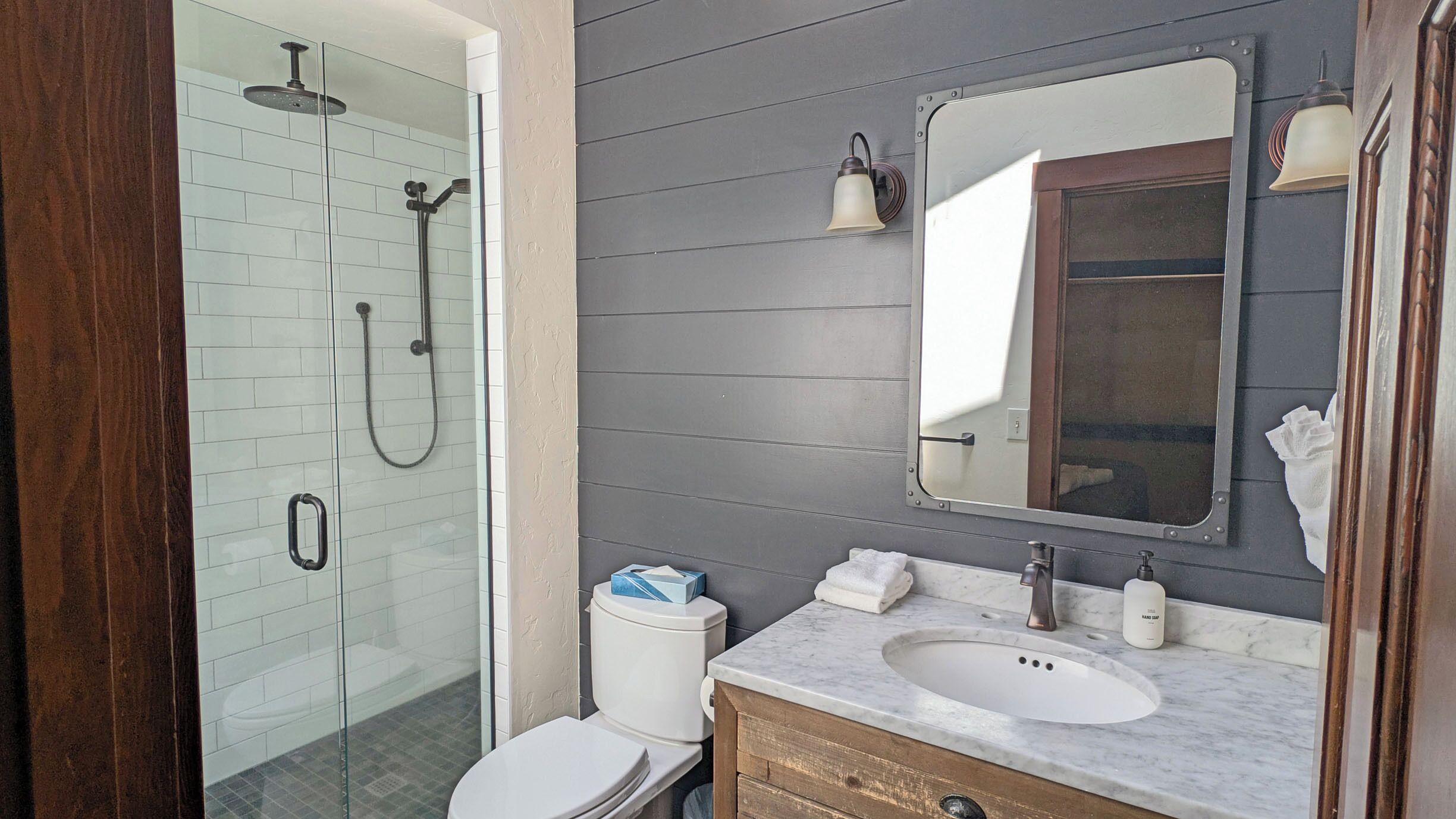 A bathroom with a glass-enclosed shower, a white toilet, a marble sink, and a mirror.