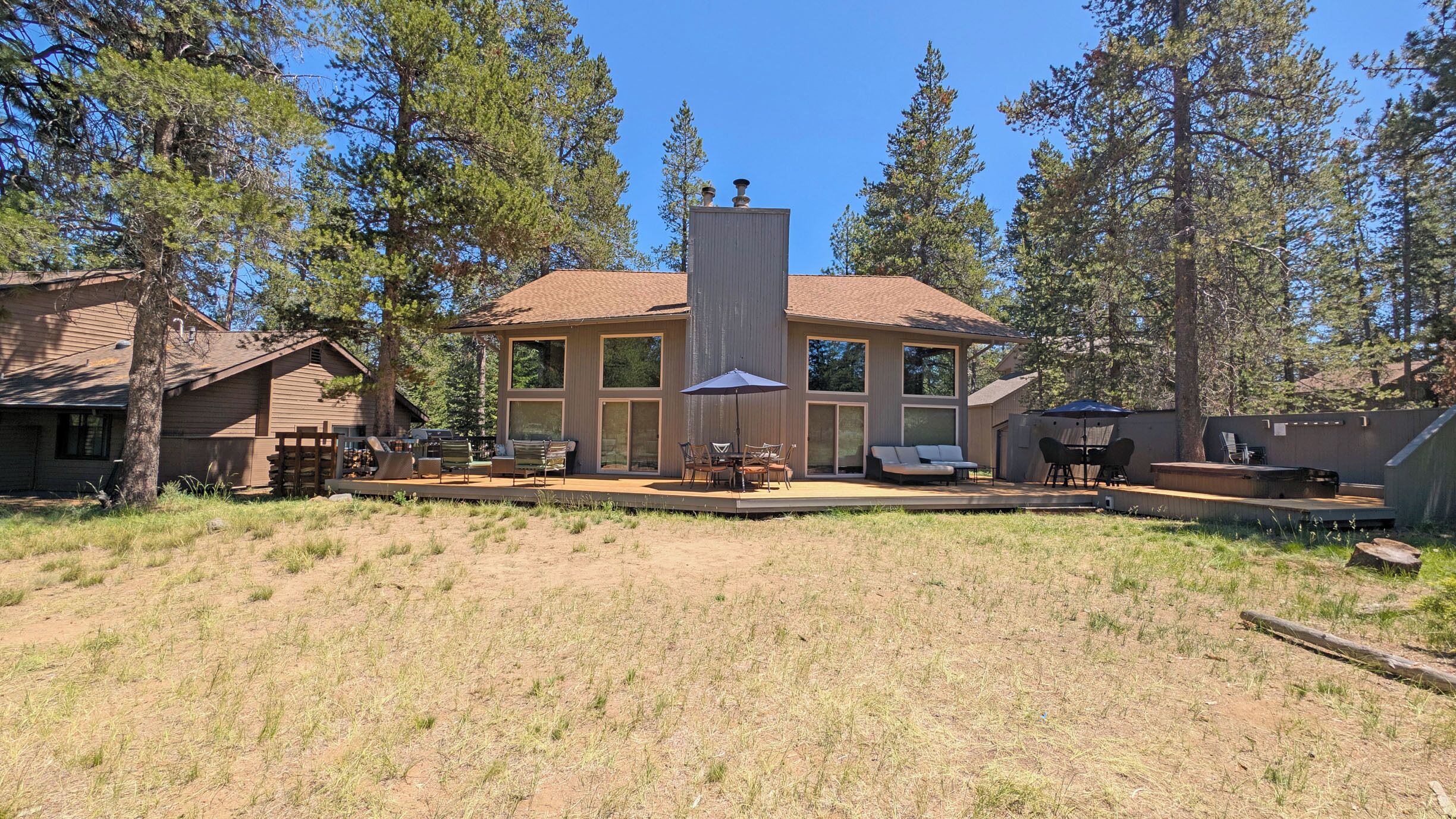 A modern house with a large deck, outdoor seating, and a chimney.
