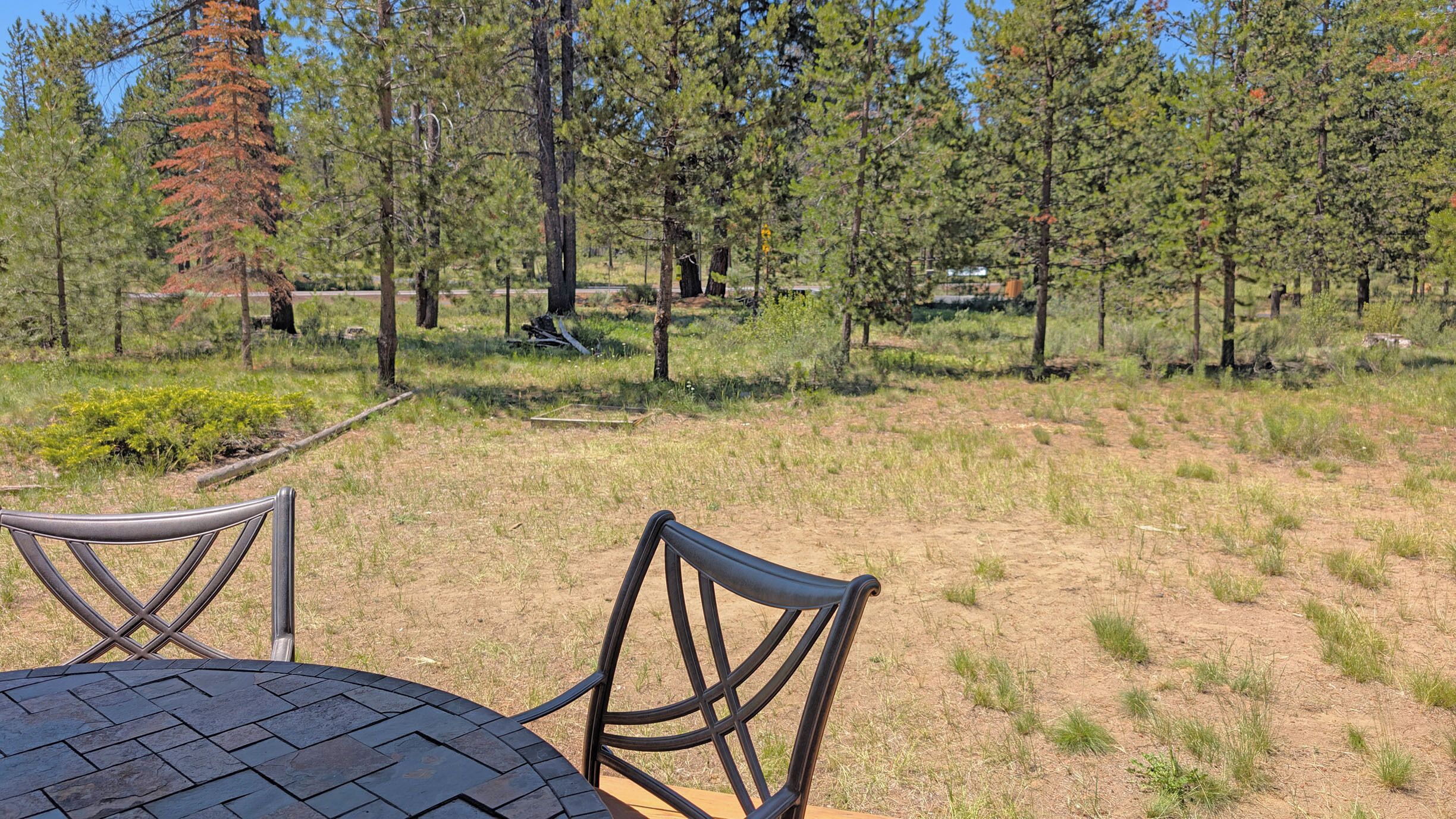 An outdoor seating area with a round table and chairs, surrounded by a natural landscape with trees and grass.