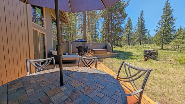 A wooden deck with outdoor furniture, a hot tub, and a view of a forest. - Indian 3 - Hot Tub, SHARC, Huge Deck, Pool Table (Sunriver)