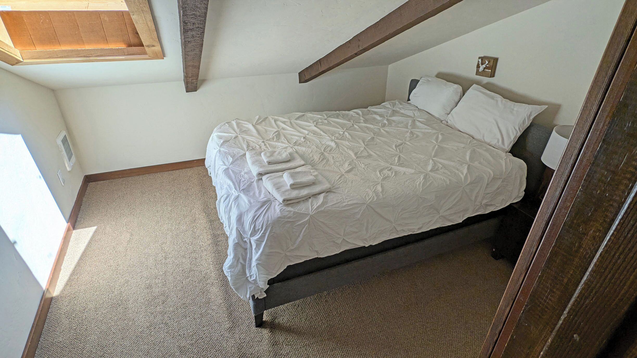 A bedroom with a bed, a nightstand, and a wooden beam ceiling.