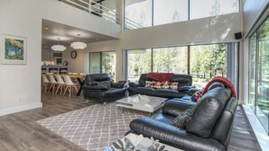 A spacious living area with a high ceiling, large windows, and a dining area with a view of the outdoors.