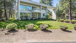 A modern two-story house with a balcony, surrounded by a well-maintained lawn and trees.