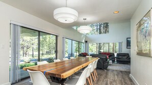 A spacious dining area with a long wooden table, white chairs, and pendant lighting.