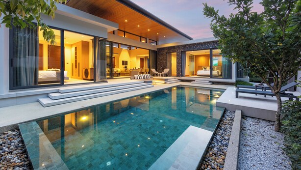 A modern house with a swimming pool, large windows, and a well-lit interior. - Exclusive Magnum Villa With Private Pool (Si Sunthon)
